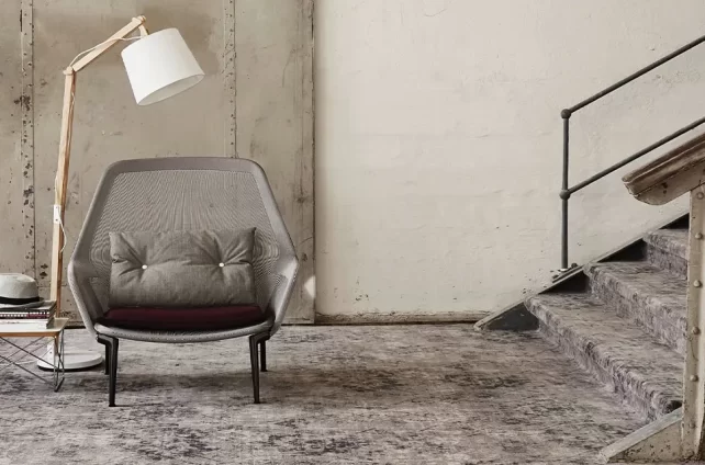 Industrieel interieur met vintage Bonaparte tapijt, designstoel, houten leeslamp en beklede trap in verweerde betonomgeving