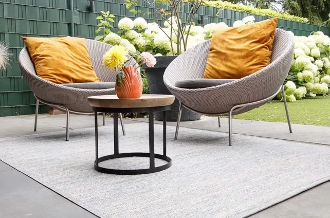 Hamat buitenkleed op een terras met ronde loungestoelen, gele kussens en bloeiende hortensia’s in een zomerse tuinsetting