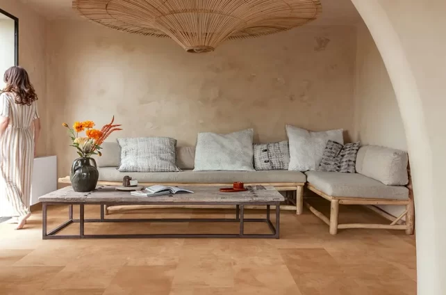 Rustige natuurlijke woonkamer met zandkleurige PVC vloer, houten bank met lichte kussens en grote rotan hanglamp.