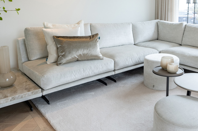 Minimalistisch interieur met zachte hoekbank, hoogpolig licht karpet en visgraat houten vloer