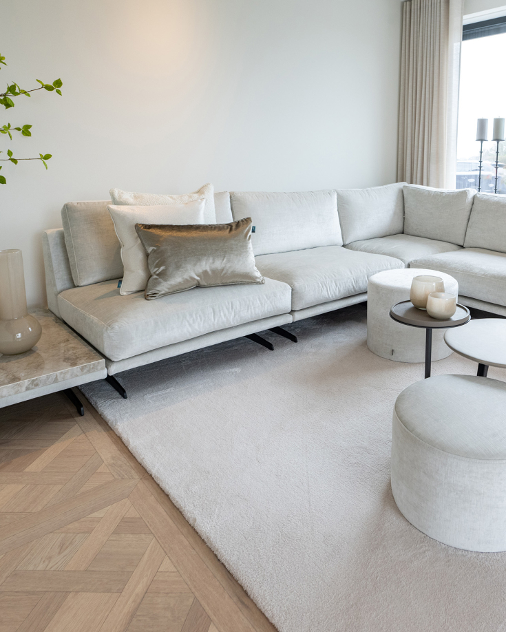 Luxe woonkamer met licht hoekbankstel, wit hoogpolig karpet en visgraat parketvloer in een elegante en rustige sfeer