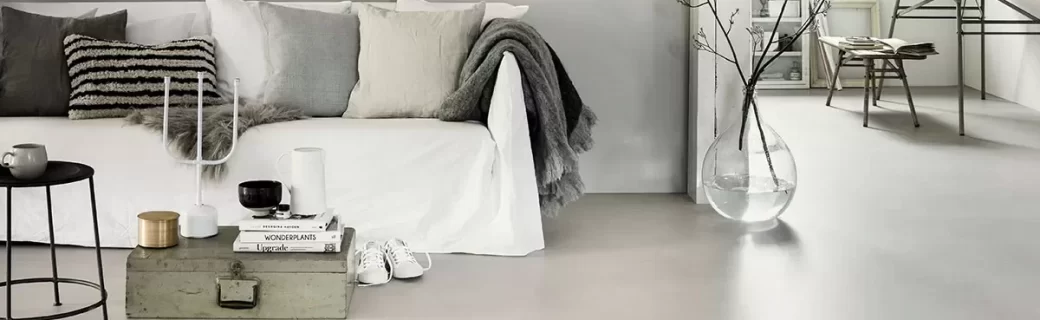 Minimalistische woonkamer met witte bank, zachte tinten en een strakke Novilon vloer in warmgrijze kleur.