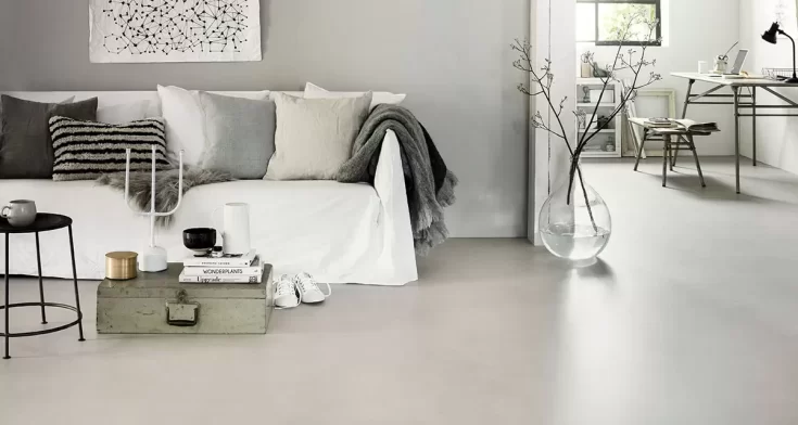 Minimalistische woonkamer met witte bank, zachte tinten en een strakke Novilon vloer in warmgrijze kleur.