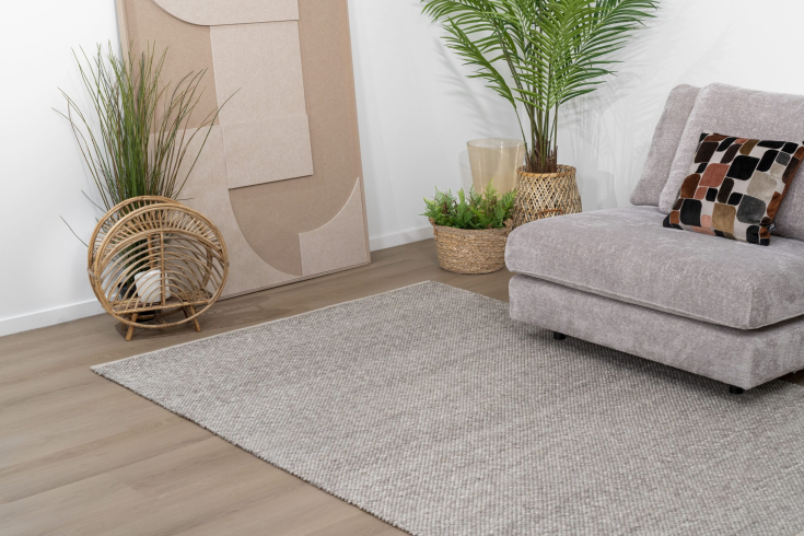 Lichtgrijs geweven karpet bij zachte hoekbank in een modern interieur met houten vloer en natuurlijke decoratie