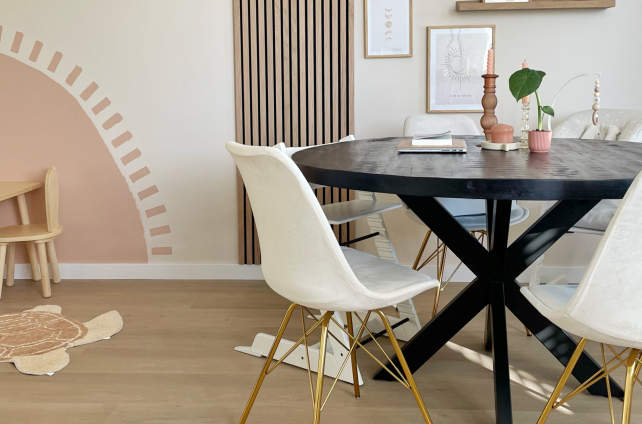 Lichte klik pvc-vloer in een Scandinavisch interieur met witgouden stoelen rond een zwart ronde tafel, decoratieve wandkunst en een kinderhoek met pastelkleuren en houten meubels.