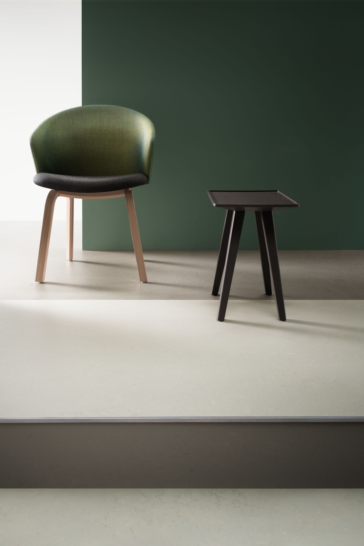 Minimalistische ruimte met lichtgrijze marmoleumvloer, groene designstoel en zwart bijzettafeltje tegen donkergroene wand