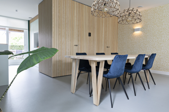 Moderne eetkamer met lichtgrijze gietvloer, houten eettafel, blauwe velvet stoelen en natuurlijke accenten in Scandinavische stijl