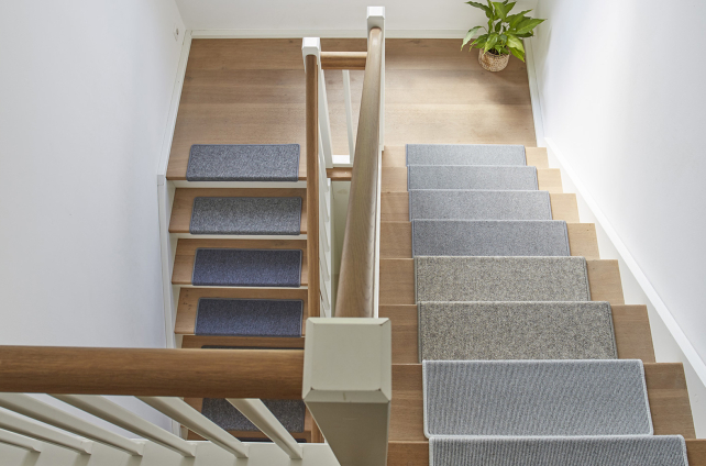 Houten trap met verschillende kleuren trapmatten en witte leuning in moderne hal