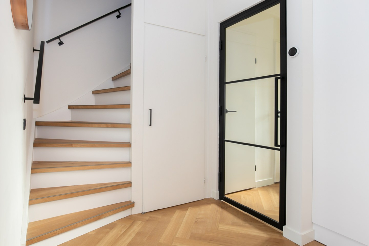Moderne hal met visgraat pvc vloer en houten trapbekleding, afgewerkt met zwarte details en een stalen binnendeur
