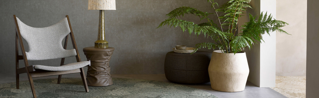 Sfeervolle zithoek met botanisch rond karpet, designstoel en grote kamerplant tegen grijze wand