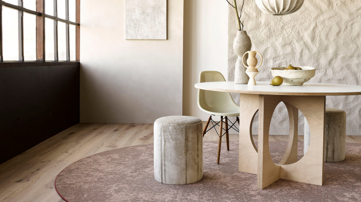 Ronde eettafel op zachtroze geweven karpet in een natuurlijk ingericht interieur met lichte houten vloer en organische accenten