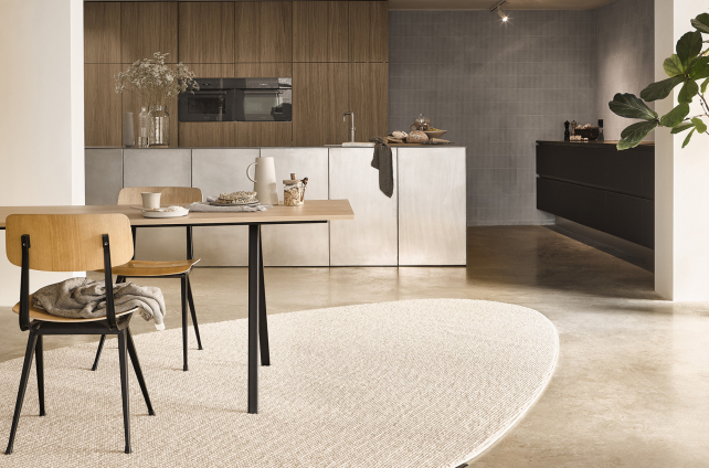 Modern interieur met lichte ovale vloerkleed, houten eettafel en strakke keuken met natuurlijke materialen