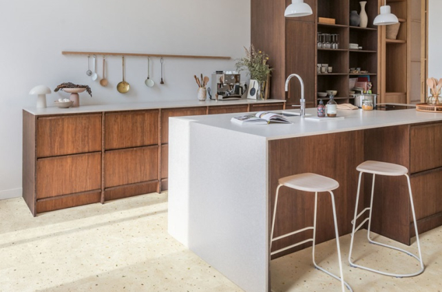 Modern ingerichte keuken met terrazzo-look vloer in zandkleurige tinten, houten keukenkasten en wit kookeiland.