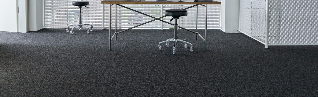 Modern kantoor met donkergrijs tapijt, metalen bureau en industriële verlichting