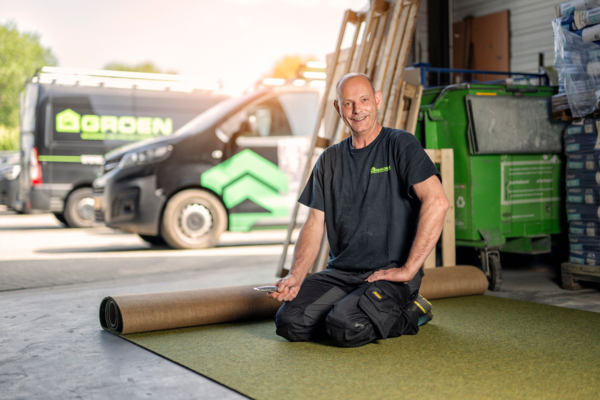 werknemer van deventervloeren van groeninrichters is bezig aan een stuk vloer in de werkplaats met groeninrichters werkbusjes op de achtergrond